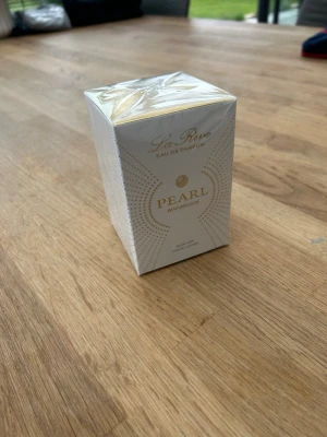 La Rive Pearl Woman Eau de Parfum - La Rive Pearl Woman Eau de Parfum i elegant vit och guld kartong. Flaskan rymmer 75 ml och doften är inspirerad av fransk parfymtradition. Förpackningen har en lyxig känsla med gulddetaljer och modern design. 