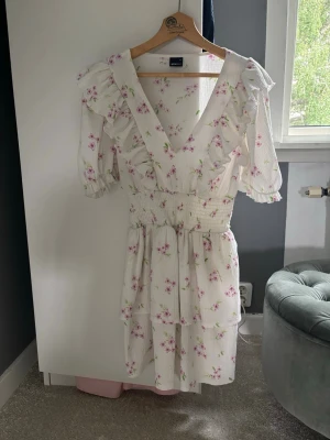 Vit blommig volangklänning  - Supersöt vit kortklänning från Gina tricot med rosa blommönster, volanger och v-ringning. Storlek xs men passar s också, endast använd 1 gång. 
