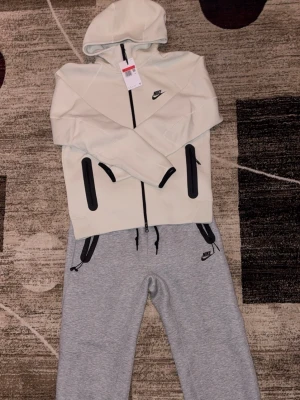 Nike Tech tracksuit - Byxan har använts max 2 gånger. Koftan har inte alls använts, etikett finns kvar. Koftan är inte snö vit. Den är mer ljus grön/vit