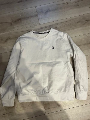 Vit sweatshirt från U.S. Polo Assn. - Klassisk vit sweatshirt med rund hals från U.S. Polo. Tröjan har en liten broderad logga på bröstet och ribbade muddar vid ärmslut och nederkant. Perfekt för en clean och enkel stil. Säljer då växt urt ur M, annars inga bekymmer 