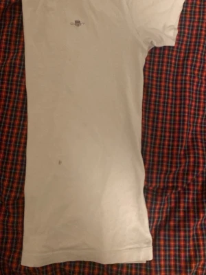 Vit t-shirt från Gant! - Vit t-shirt från Gant. Tröjan har diskreta ränder på ärmsluten. Klassisk passform och rund halsringning, perfekt för en clean och enkel stil. Den är lite för liten för mig de derför jag säljer denna tröja. Den har också en liten fläck men den syns inte så mycket:) pris kan diskuteras👌