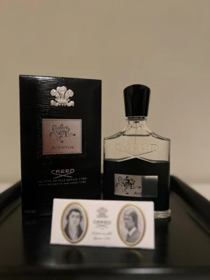 Creed Aventus Eau de Parfum 100ml - Lyxig parfym från Creed, Aventus, i en elegant genomskinlig glasflaska med svart och silverdetaljer samt svart kork. Flaskan rymmer 100 ml och kommer med originalförpackning. Doften är ikonisk och exklusiv, perfekt för dig som gillar unika och sofistikerade parfymer.