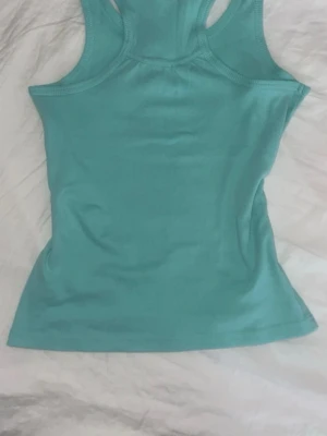 Turkos linnetopp från Warp - Snygg turkos linnetopp från Warp med brottarrygg och tight passform. Tillverkad i mjuk bomull som känns skön mot huden. Perfekt till sommaren och enkel att matcha med jeans eller shorts.