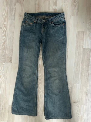 Blå bootcut jeans från Weekday - Säljer ett par klassiska blå bootcut jeans från Weekday med fem fickor och snygga slitningar. Jeansen har normal midja, dragkedjegylf och är tillverkade i slitstark denim. Perfekta för dig som gillar en avslappnad men trendig look.