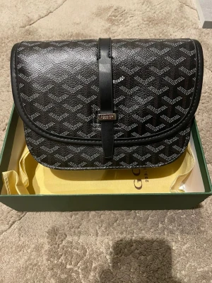 Svart axelväska - Snygg svart axelväska med deras ikoniska mönster i vitt och grått. Väskan har en rundad form, lock med spänne och detaljer i svart läder. Perfekt för dig som gillar exklusiva accessoarer och vill sticka ut med en klassisk design. Har i grön färg också båda kommer med packet och dustbag 