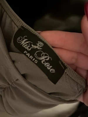 Grå volangtopp från Miss Rose Paris - Supersnygg grön topp från Miss Rose Paris med volangdetalj nedtill. Toppen har en elegant, figurnära passform och är tillverkad i ett mjukt, glansigt material som ger en lyxig känsla. Perfekt att styla med jeans eller kjol för en trendig look. Pris kan diskuteras 