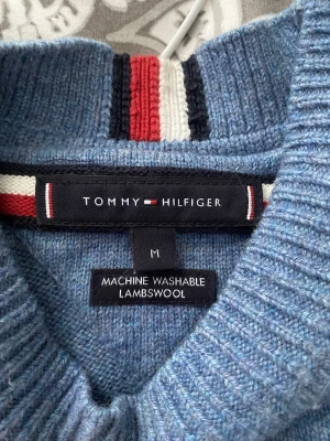 Blå stickad tröja Tommy Hilfiger - Snygg blå stickad tröja från Tommy Hilfiger i mjuk lammull. Tröjan har rund halsringning, ribbade muddar och en liten broderad logga på bröstet. Perfekt för dig som gillar klassisk och stilren design.
