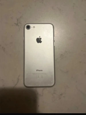 Silver iPhone 7 - Säljer en silverfärgad iPhone 7 från Apple. Telefonen har en stilren design i aluminium, rund hemknapp med Touch ID och en enkel bakre kamera. Klassisk Apple-logga på baksidan och svart framsida med vit ram. Perfekt för dig som gillar smidig och snygg mobil. Har dock en liten spricka på vänster kanten, men annars fungerar utmärkt
