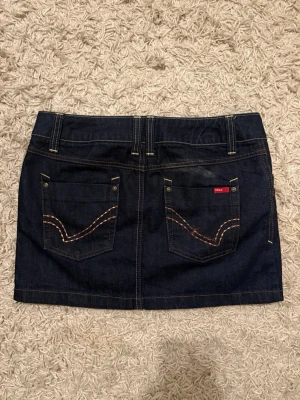 Mörkblå jeanskjol från Only - Snygg mörkblå jeanskjol från Only med brodering på fickorna🥰har aldrig använt den och måttet på längden är 35 cm!