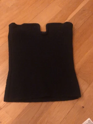 Svart stickad topp med unik halsringning - Säljer en svart stickad topp med kort ärm och en cool, fyrkantig halsringning med liten urgröpning i mitten. Toppen har en figurnära passform och är gjord i ett mjukt, stickat material. Perfekt för dig som gillar stilrena och trendiga plagg.