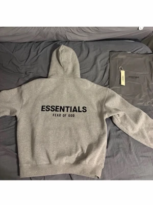 Grå Essentials Hoddie  - Riktig snygg grå hoddie från Essentials med svart logga på ryggen och bröstet🔥perfekt skick, den har väldigt bra passform, ja är ca 180 och väger runt 78 och den passar perfekt🔥snabb Affär=bättre pris🔥🔥 du får med original zip bag och tags.