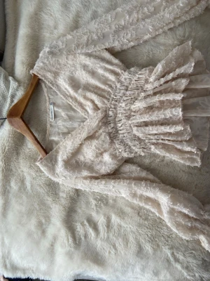 Beige/rosa  blus från Bisous Project - Supersöt beige blus från Bisous Project med v-ringning och smockad midja. Blusen har långärmade ärmar med volangdetaljer. 