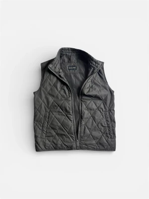 Svart quiltad dunväst (Massimo Dutti) - Stilren svart dunväst från Massimo Dutti med quiltat mönster och hög krage. Västen har dragkedja framtill och två sidofickor. Perfekt att slänga över en hoodie eller tröja för extra värme och en clean look.