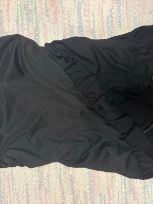 Svart kortkjol med volangkant - Säljer en svart kortkjol med volangkant nedtill. Kjolen har en enkel och stilren design med resår i midjan för skön passform. Perfekt att matcha med en crop top eller stickad tröja för en trendig look.