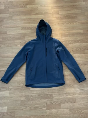 Blå skid/vandringsjacka Peak Performance storlek L - Snygg blå skid/vandringsjacka från Peak Performance med hjälmkompatibel huva och hel dragkedja framtill. Jackan har tre fickor med dragkedja och diskret logga på bröstet. Tillverkad i ett slätt, vattenavvisande material som passar perfekt för blåsiga dagar. Bra skick, fåtal mycket små fläckar. Nypris 2400kr säljs för 1000. Modellen heter ”M Xenon Jacket Blue Steel”.