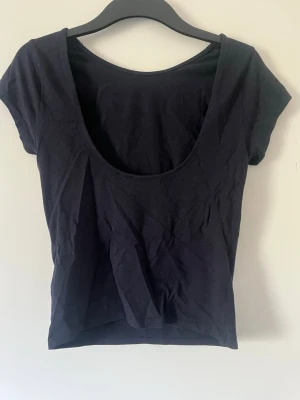 Svart t-shirt med öppen rygg - En svart, enkel t-shirt med korta ärmar och en lite öppen rygg. Tillverkad i mjuk bomull, perfekt för en avslappnad och stilren look. Passformen är normal och toppen är enfärgad utan mönster eller detaljer.