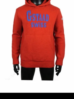 Moncler Hoodie - Unik Moncler hoodie i storlek M. Tröjan är orange och stickad i kashmir. Tröjan har huva, magficka och ribbade muddar vid ärmslut och nederkant. Framtill finns blå text med "Gstaad Swiss" och på ärmen sitter en Moncler-logotyp. Passar som varm och mjuk vardagströja eller mellanlager i kallare väder.  Upplever tröjan något för stor för min smak.  Inköpt i en av de två Moncler (Grenoble) butikerna i St.Mortiz för 4år sedan för 799 SFr. NFC, denna version går ej att hitta som fejk. 