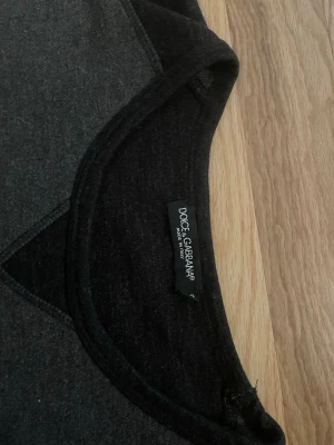 Mörkgrå sweatshirt från Dolce & Gabbana - Snygg mörkgrå sweatshirt från Dolce & Gabbana med svarta ärmar och diskret logotyp på bröstet. Tröjan har rund halsringning och är tillverkad i mjukt material som känns skönt mot huden. Perfekt för en avslappnad och trendig look.
