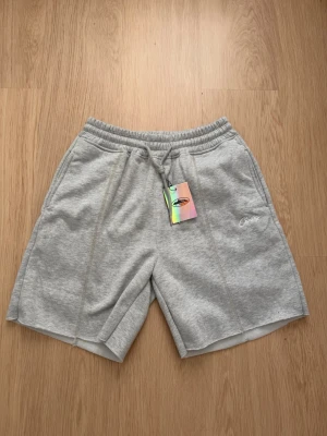 Grå sweatshorts från Corteiz - Säljer ett par grå sweatshorts från Corteiz med broderad logga på vänster ben. Shortsen har elastisk midja med snörning och två sidofickor. Perfekta för chill dagar och har en relaxed fit.