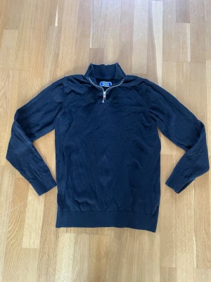 Svartstickad tröja med halvzip - Snygg Svart stickad tröja  med halvzip och hög krage. Tröjan har långa ärmar, ribbade muddar och nederkant. Perfekt för lager på lager och stilrena outfits. Tröjan är även i nyskick och aldrig använd
