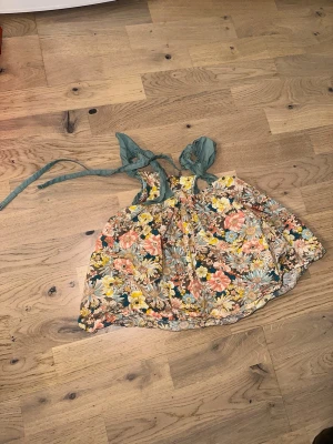 Blommig kortklänning med knytband - Superfin kortklänning med färgglatt blommönster i gult, rosa, blått och grönt. Klänningen har gröna knytband vid axlarna och en luftig passform. Perfekt för varma dagar och ger en härlig sommarkänsla.