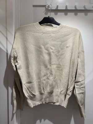 Beige stickad tröja från Stussy | S - Snygg beige stickad tröja från Stussy med broderad logga på bröstet. Tröjan har rund halsringning, ribbade muddar och är tillverkad i ett mjukt, grovstickat material. Perfekt för lager-på-lager och chill stil. Använd endast 1 gång!