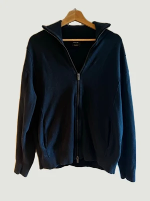 Marinblå ziptröja från Massimo Dutti - Stilren marinblå ziptröja från Massimo Dutti med hög krage och tvåvägsdragkedja. Tröjan har ribbade muddar och fickor på sidorna. Perfekt för lager-på-lager och enkel att matcha med andra plagg.