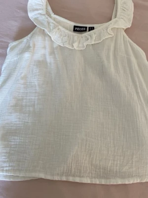 Vit linnetopp med volang från vero Moda  - Söt vit linnetopp från vero Moda med volangdetalj runt halsringningen. Toppen är ärmlös och har en luftig, lätt struktur som passar perfekt till varma dagar.💓💓