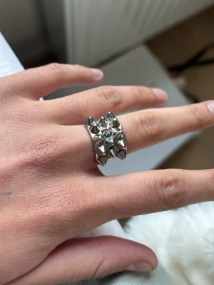 Silvrig ring med nitar - Cool och chunky ring i silverfärgad metall med flera små pyramidformade nitar runt hela ringen. Ringen har en bred design och ger en edgy känsla, perfekt för dig som gillar statement-smycken.