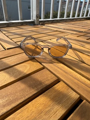 Transparenta solglasögon med bruna glas - Snygga solglasögon med transparent plastbåge och bruna glas. Modellen har en modern, kantig form som ger en cool vibe. Perfekta för att lyfta din stil under soliga dagar.