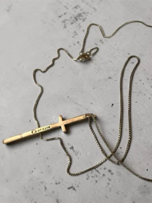 Guldfärgat halsband med kors - Snyggt halsband i guldfärg från Emma Israelsson  med ett stilrent kors som hänge. Kedjan är tunn och har en klassisk låsning. Perfekt för dig som gillar minimalistiska smycken med en modern touch.