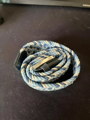 Blått flätat bälte från ONEWear - Snyggt flätat bälte från ONEWear i olika blå nyanser och beige. Bältet har silverfärgat spänne och detaljer i skinn. Perfekt för att ge din outfit en cool touch.