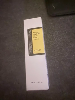 COSRX Advanced Snail 96 Mucin Essence - En populär toner från COSRX med snigelsekret, Advanced Snail 96 Mucin Power Essence. Kommer i en vit rektangulär förpackning med gul etikett. Innehåller 100 ml och är perfekt för återfuktning och glow.
