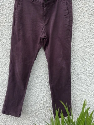 Plommonlila chinos från Uniqlo - Snygga plommonlila chinos från Uniqlo med klassisk rak passform och fickor i sidorna. Byxorna är tillverkade i 97% bomull och 3% elastan för en skön stretchig känsla. Perfekta för dig som vill ha en stilren och bekväm look.