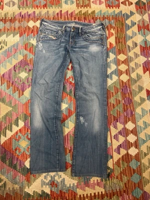 Blå bootcut jeans med slitningar - Snygga blå bootcut jeans med ljusa slitningar och klassiska fem fickor. Jeansen har kontrastsömmar och en låg midja. Perfekta för en avslappnad och trendig look.