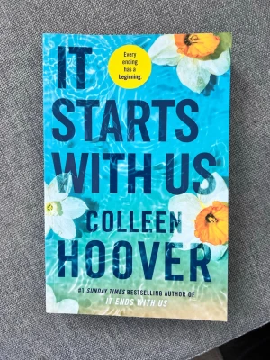 It Starts With Us av Colleen Hoover - En färgstark pocketbok med blått omslag och blommor, skriven av Colleen Hoover. Boken är en uppföljare till 'It Ends With Us' och handlar om relationer, kärlek och nya chanser. Perfekt för dig som gillar romantisk och känslosam skönlitteratur.