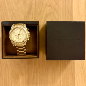 Guldig klocka från Michael Kors - Stilren guldig klocka från Michael Kors med strass  runt boetten, lite y2k stil. Använt men ändå väldigt bra skick med få tecken på användning, se bild. 