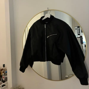 Skinn bomberjacka från Pull&Bear - Snygg svart skinn bomberjacka från Pull&Bear med silvriga dragkedjor och en ficka på bröstet. Jackan har klassisk bombermodell med ribbade muddar och krage. Perfekt för dig som vill ha en stilren och trendig look.