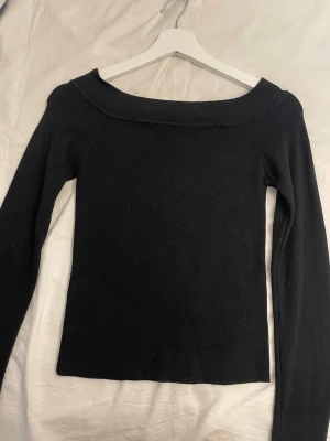 Svart off shoulder stickad tröja - Svart stickad tröja från Pull&Bear med off shoulder-ringning och långa ärmar. Tröjan har en enkel, tight passform och är tillverkad i mjukt stickat material. Perfekt för en stilren och trendig look.