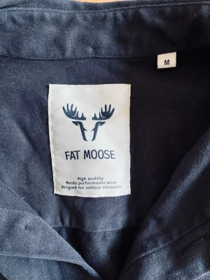 Mörkblå skjorta från Fat Moose - Stilren mörkblå skjorta från Fat Moose i bomull. Skjortan har klassisk krage, bröstficka och knäppning framtill. Perfekt för dig som gillar enkel och clean stil.