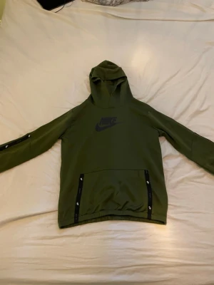 Olivgrön Nike hoodie - Snygg olivgrön hoodie från Nike med svart logga på bröstet. Och en stor magficka. Perfekt för en sportig och avslappnad stil.