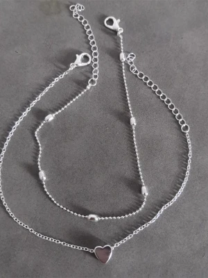 Fotlänk  - 2 delar: 1 st dekorerad med ett hjärta. 1 st dekorerad med kulor. Materialet är alloy. (#270)