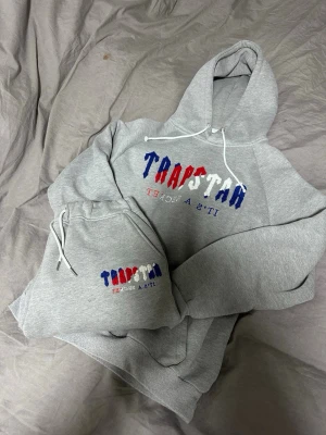 Trapstar Dress - Säljer en grå dress från Trapstar i storlek XL(Passar som L). Hoodien har huva med dragsko och tryck framtill i blått, rött och vitt där det står 'TRAPSTAR It's A Secret'. Tvär skön fleece på insidan, minns ej vilket drop den är ifrån men rätt så gammalt, hör av er vid frågor/funderingar! ✌️