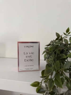 Lancôme La Vie Est Belle EdP 30ml - Lancôme La Vie Est Belle Eau de Parfum i en elegant, rektangulär rosa och vit kartong. Doften är känd för sin söta och blommiga karaktär och kommer i en 30 ml förpackning. Perfekt för dig som gillar lyxiga och feminina parfymer.