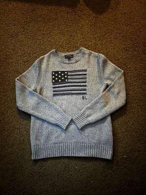 Grå stickad tröja från Polo Ralph Lauren - Ljus blå stickad Polo Raulph lauren tröja med Amerikansk flagga på bröstet.         Kom privat för mer bilder eller information. 
