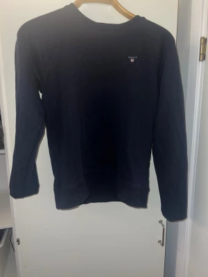 Mörkblå sweatshirt från Gant - Mörkblå sweatshirt från Gant med rund halsringning och diskret logga på bröstet. Tröjan har långa ärmar och är tillverkad i mjukt material som passar perfekt till en avslappnad stil.