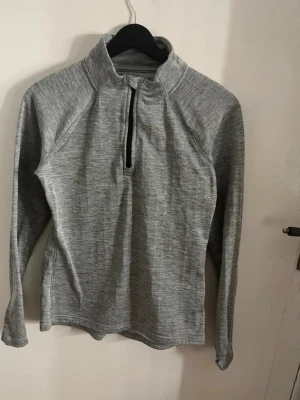 Grå långärmad sporttröja med dragkedja - Snygg grå långärmad sporttröja med halv dragkedja framtill och hög krage. Perfekt för träning eller löpning. Tillverkad i mjukt och stretchigt material som andas. Enkel och stilren design som passar till det mesta inom sport. Säljer även de rosa tränings byxorna/tightsen! 