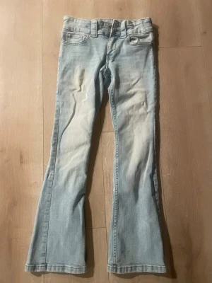 Ljusblå bootcut jeans med fickor - Snygga ljusblå jeans med bootcut passform och klassiska fem fickor. Jeansen har hällor för bälte och knäppning fram. Materialet är denim med en lätt tvättad look och bakfickor med lock och knapp.