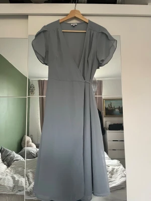 Ljusblå omlottklänning  - Snygg ljusblå långklänning med omlottmodell och v-ringning. Använt 1 gång! Passar till bröllop, finmiddagar eller när du bara vill vara extra snygg!