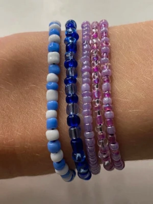Färgglada pärlarmband i blått och lila - Fem elastiska armband med små pärlor i olika färger. Två armband är blå och vita, ett är genomskinligt blått och två är lila och rosa. Perfekt för att ge din stil en färgklick och personlig touch. Ett för 10kr (typ). Säljer i fler färger. 